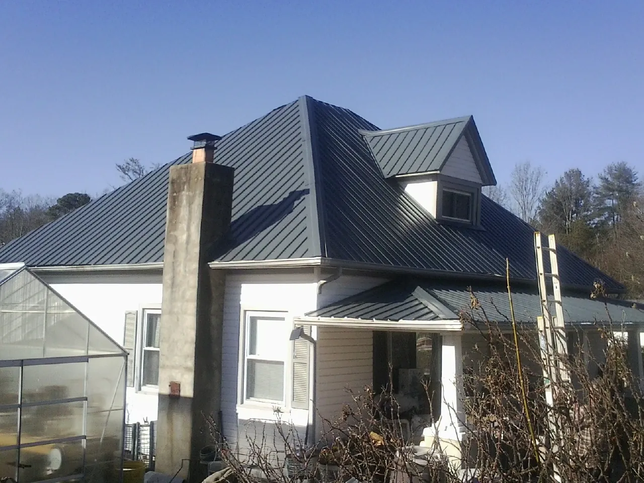 Dark blue standing seam metal roof on a white farmhouse with dormer — Slate & Tile Roof Repair by Roofing Brothers in Criders