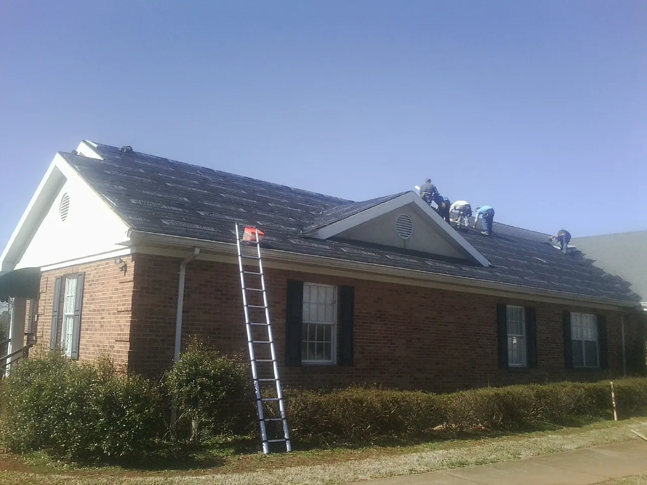 Crew tearing shingles off a brick ranch roof with a ladder set — Emergency Roof Repair work by our crew in Criders