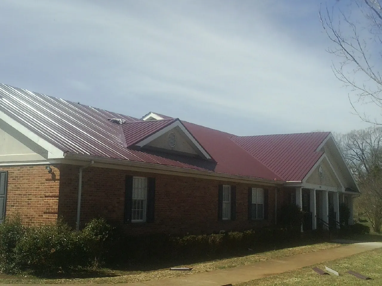 Red metal roof with gabled entries on a long brick building, from a Hail Damage Roof Repair job in Criders