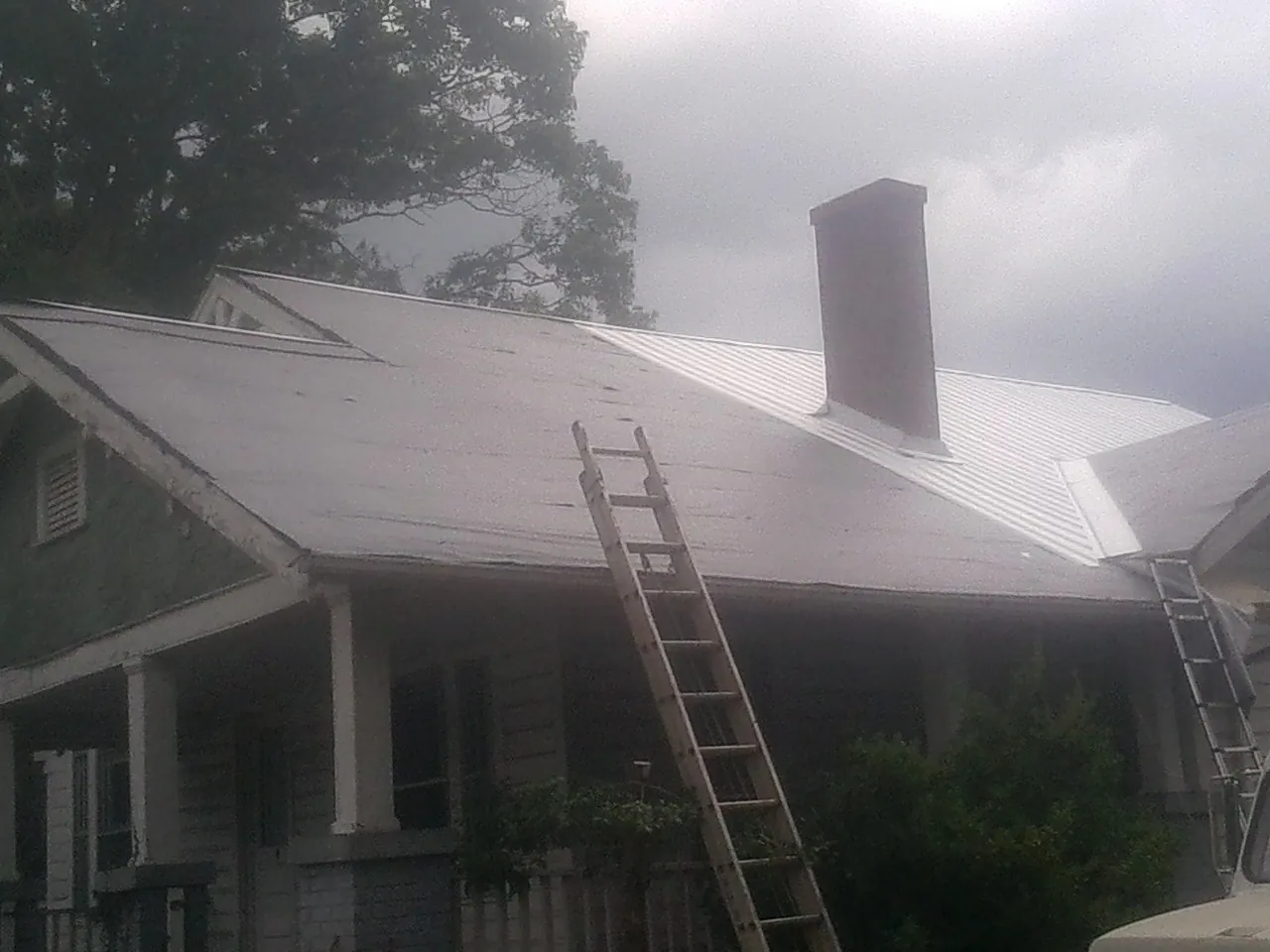 Ladders against a metal roof on an older home with a brick chimney in Criders