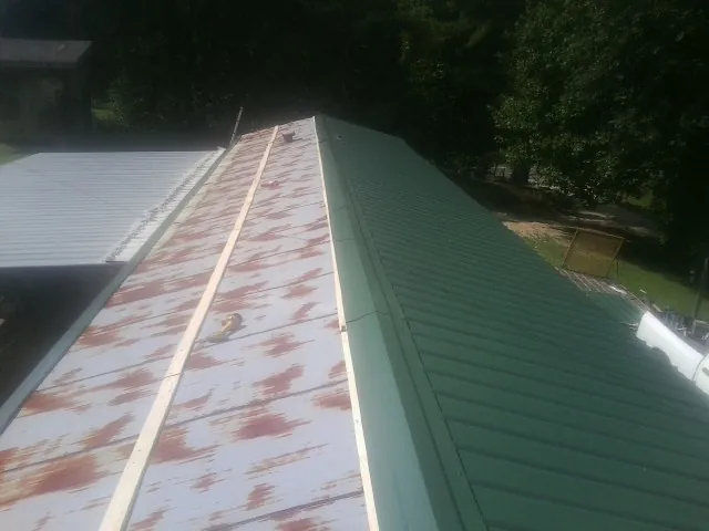 Old rusted panels beside newly installed green metal roofing — Wind Damage Roof Repair by Roofing Brothers in Criders