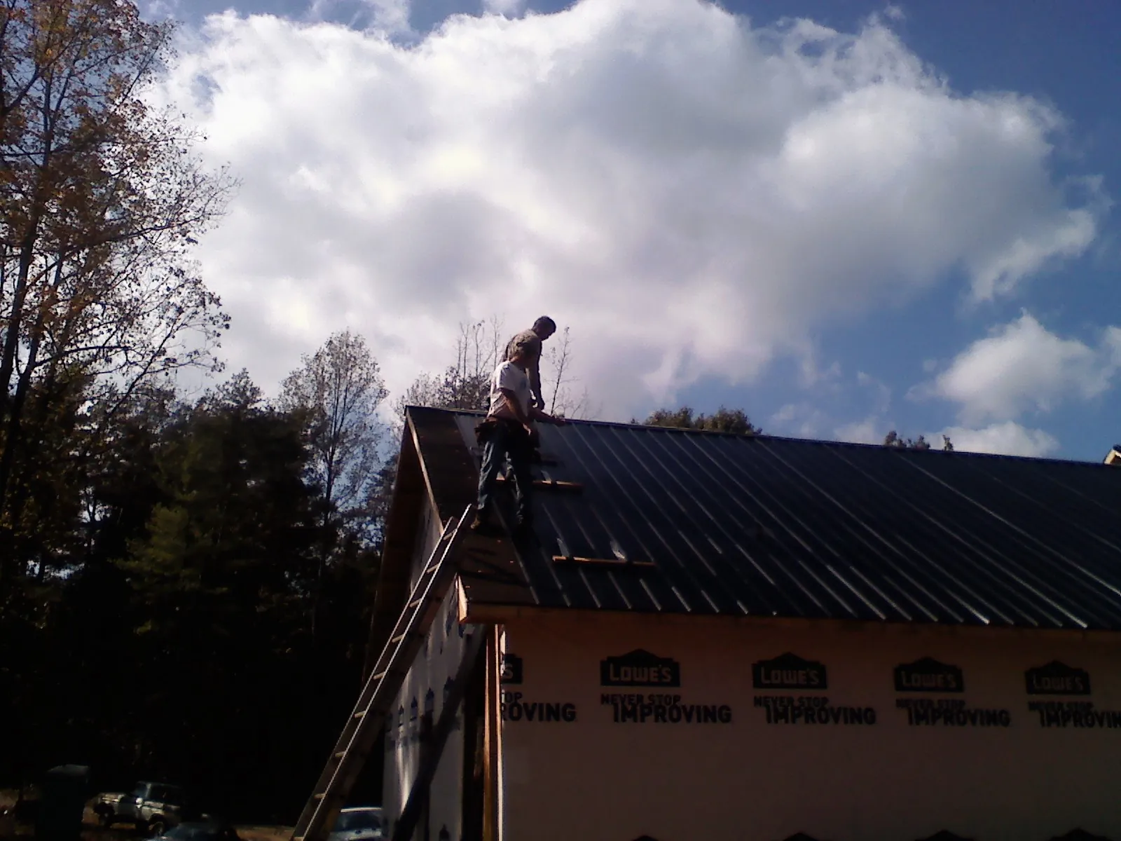 Roofer fastening dark metal panels high against a cloudy sky, from a Roof Inspection job in Criders